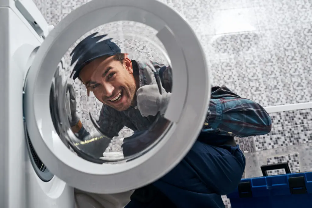 Working man plumber in bathroom checking work of washing machine close-up